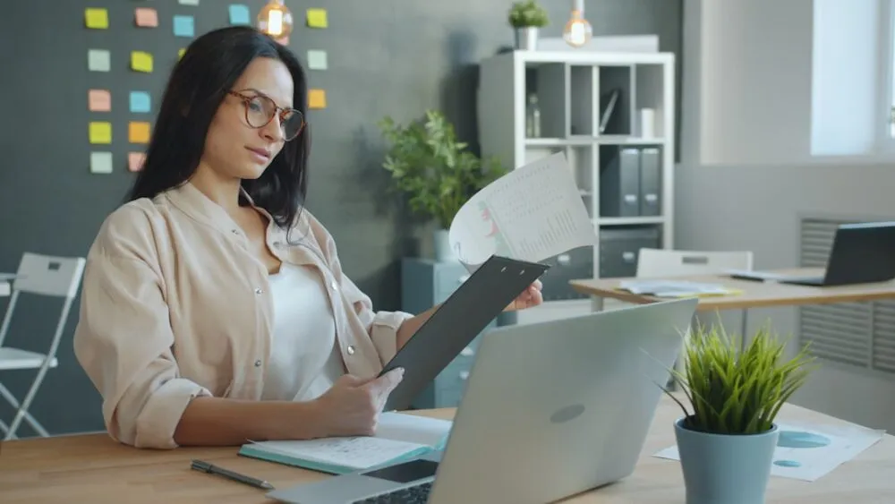 HR Manager ชาวเอเชียกำลังใช้ AI ช่วยคัดกรอง Resume ผู้สมัครบนหน้าจอแล็ปท็อปในสำนักงาน